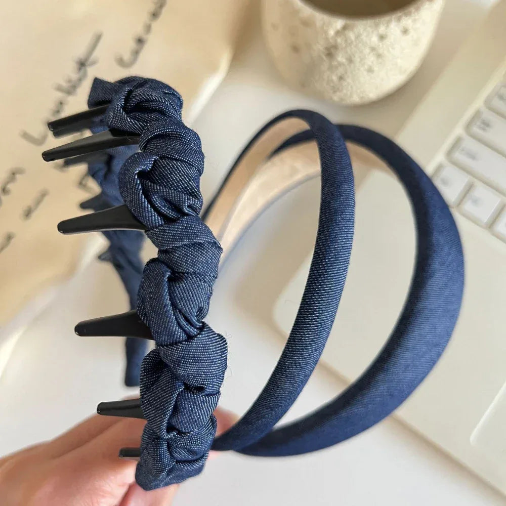 A hand holding a denim headband with knotted fabric and clips, next to a padded denim headband.
