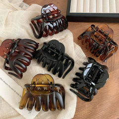 flat lay of six hair claw clips in black and tortoise shell patterns on a white cloth and wooden surface