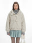 Close-up of a cream fuzzy hooded bomber jacket with toggle closure, worn over a grey turtleneck and a light blue pleated skirt.