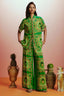 Full-length view of a woman in a green printed silk pajama set, showcasing the matching top and wide-leg pants.