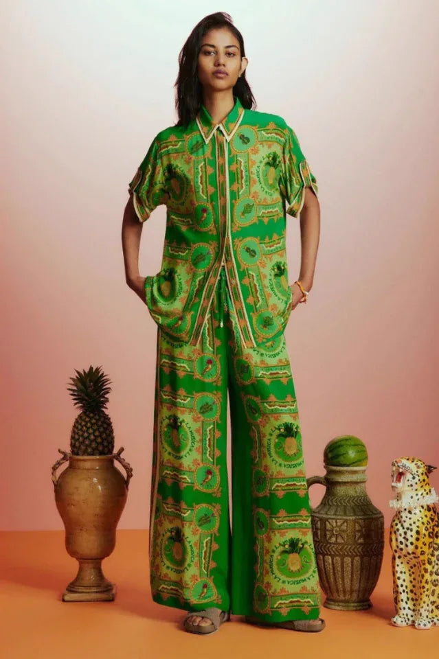 Full-length view of a woman in a green printed silk pajama set, showcasing the matching top and wide-leg pants.