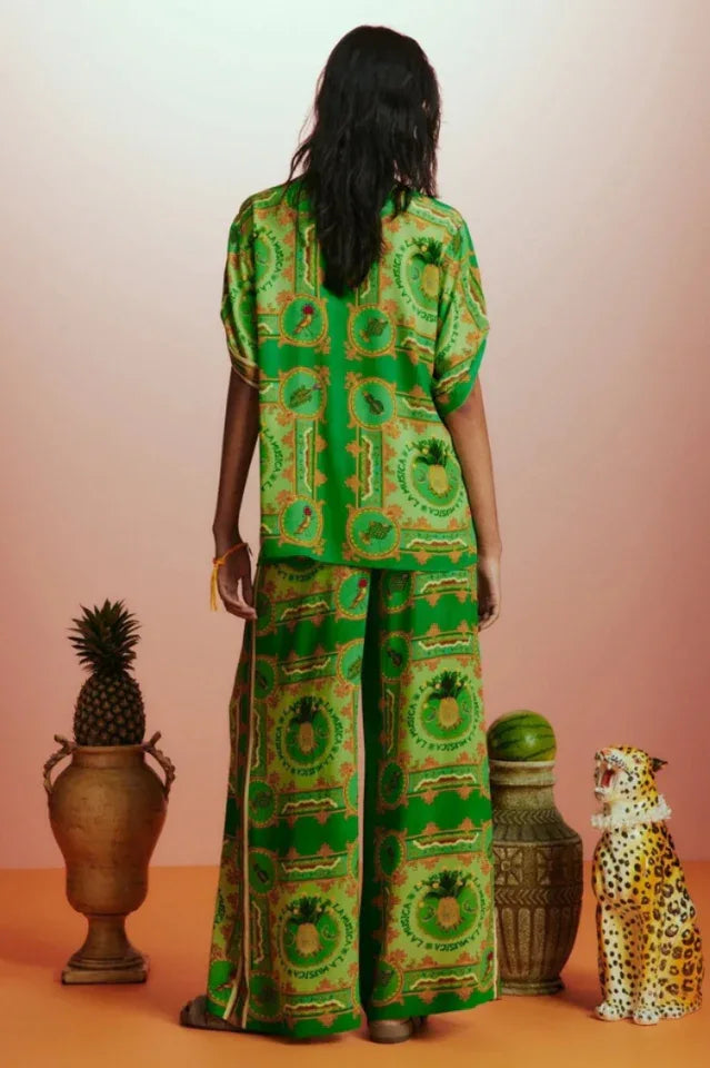 Rear view of a woman in a green printed silk pajama set, showing the back of the short-sleeve shirt and wide-leg pants.