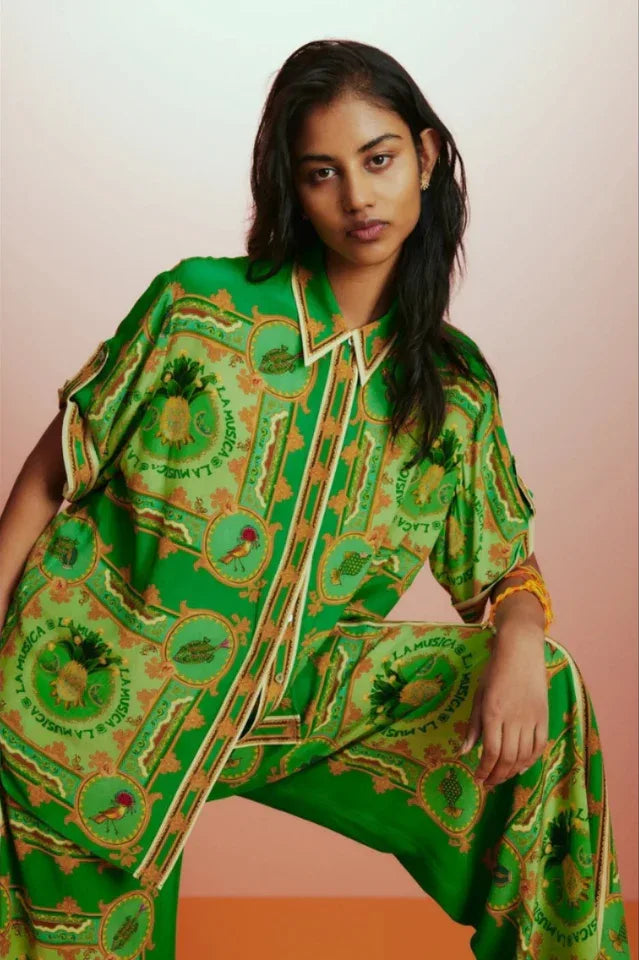 Close-up of a woman wearing a green printed silk pajama top, highlighting the intricate pattern and camp collar.