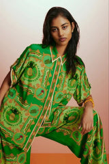 Close-up of a woman wearing a green printed silk pajama top, highlighting the intricate pattern and camp collar.