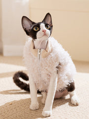 Black and white cat wearing a white sherpa fleece vest with a zipper closure and a tan ribbed collar.