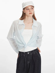 Woman wearing a light blue sheer button-down shirt tied at the waist over a white tube top, dark wash wide-leg jeans, and a white and blue striped headscarf.