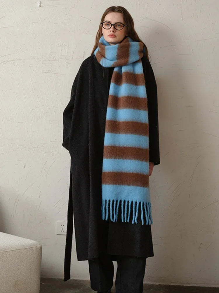 Woman standing with a black coat and a blue and brown striped scarf draped around her neck