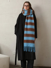 Woman standing with a black coat and a blue and brown striped scarf draped around her neck