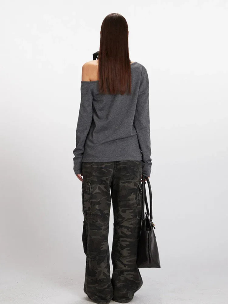 Back view of a model in a grey off-the-shoulder knit top and camouflage cargo pants.