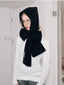 Woman wearing a black hooded scarf with a large bow detail and a white long-sleeved shirt.