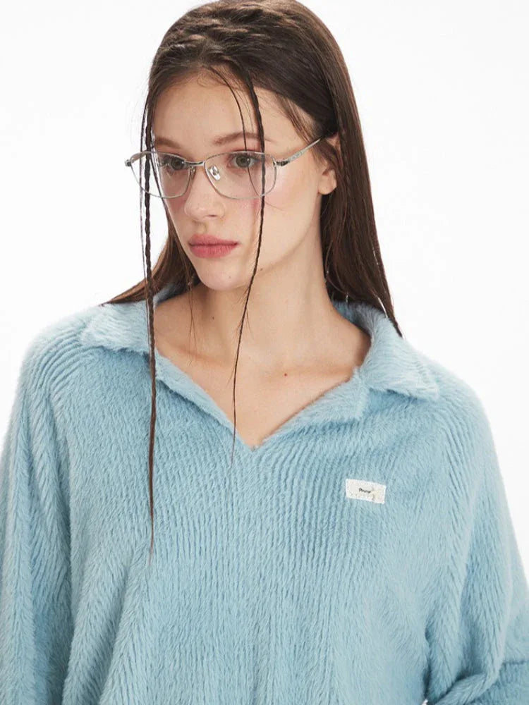 Close-up of a model's face wearing a light blue fuzzy knit collared v-neck sweater and silver-rimmed glasses.