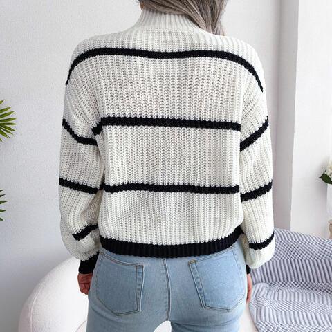 Back view of a woman wearing a white and black striped knit sweater with a high neckline and long sleeves, paired with light blue jeans.