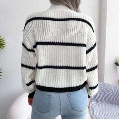 Back view of a woman wearing a white and black striped knit sweater with a high neckline and long sleeves, paired with light blue jeans.