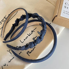 Two denim headbands, one padded and one with knotted fabric and clips, on a cloth.