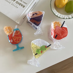 overhead view of four acrylic cocktail hair clips arranged on a white surface with books and fruit