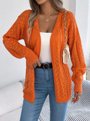Woman holding a cream clutch and wearing an orange open-front knit cardigan over a white tank top and blue jeans.