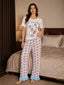 Front view of a woman wearing a white short-sleeve pajama top with a cartoon cat graphic and white pajama pants with a pink bow print and blue ruffle hem, standing in a bedroom.