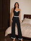 Front view of a woman wearing a black pajama set with white lace trim and a bow detail, standing in a bedroom.