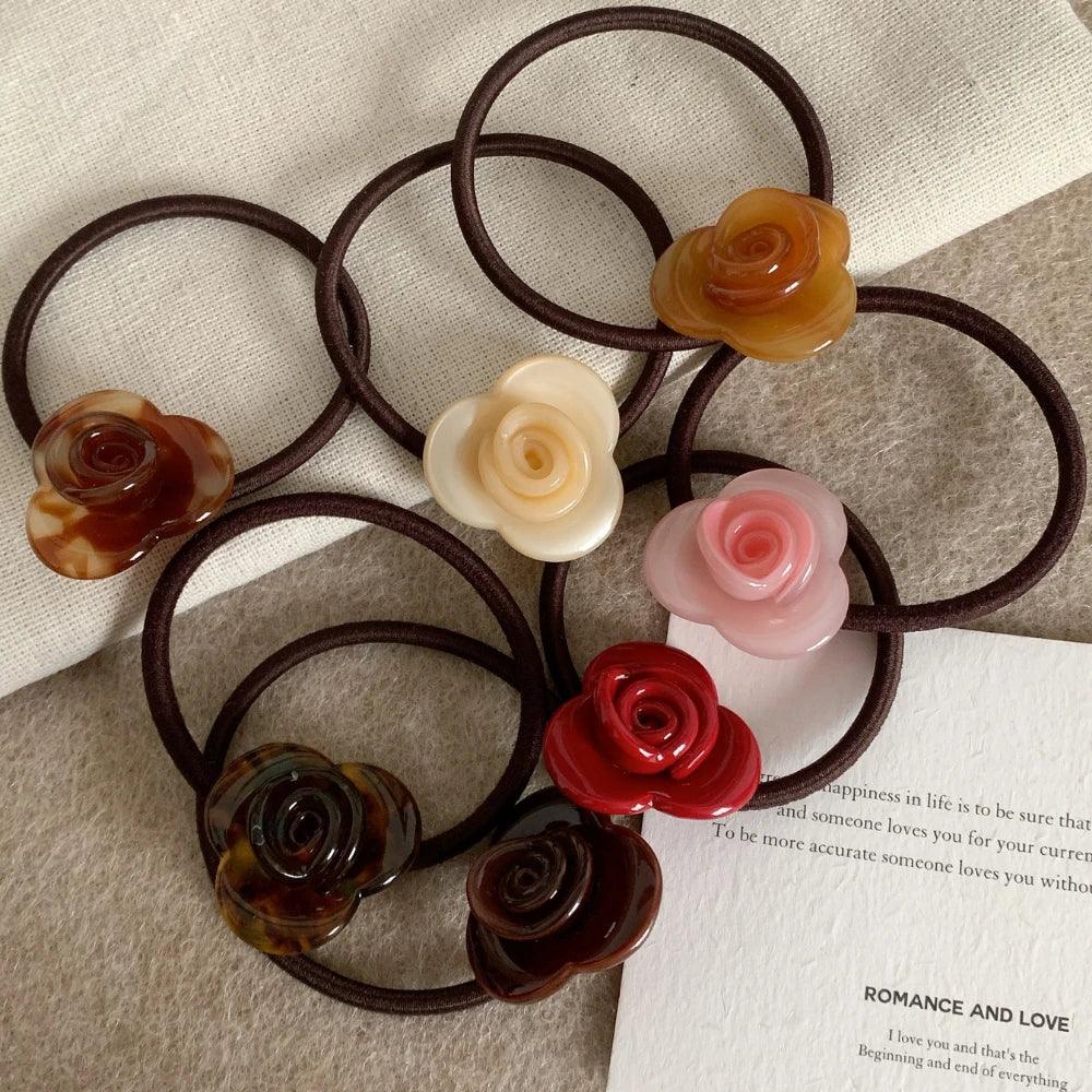 Several rose-shaped hair ties are scattered on a textured surface, with a piece of paper containing text in the background.