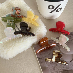 Various acetate claw hair clips arranged on a textured surface, with a coffee cup in the background
