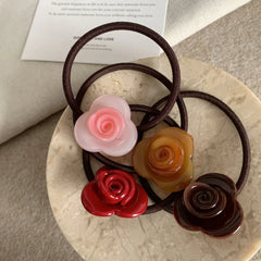 A close-up view of four rose-shaped hair ties with different colored flower embellishments, arranged on a decorative plate.