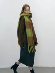 Woman walking in a brown sweater, grey skirt, black boots, and a green and brown plaid scarf.
