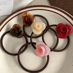 A top-down view of six rose-shaped hair ties with various colored flower embellishments, presented on a white plate.