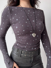 Model from the chest down wearing a grey long-sleeve top with a white star print and a heart-shaped locket.