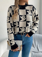 Woman wearing a black and white ghost print checkerboard knit sweater with blue jeans and a white clutch bag.