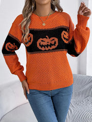 Woman posing in an orange and black pumpkin print knit sweater and blue jeans, holding a handbag chain