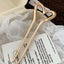 A gold-tone heart-shaped hairpin placed on white tissue paper over a textured brown fabric, with a piece of paper featuring text in the background.