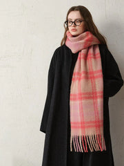 Woman wearing a black coat and a pink plaid scarf, standing against a textured wall.