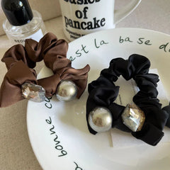 Two satin scrunchies, one black and one brown, with decorative embellishments, placed on a plate