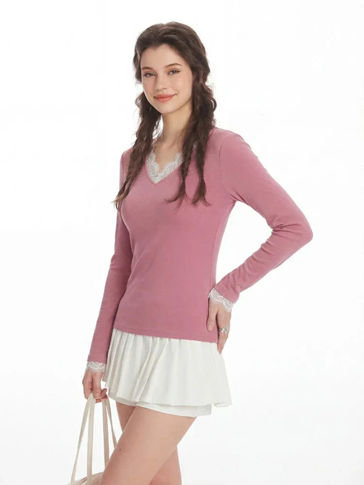 Close-up of a woman wearing a pink long-sleeved top with white lace trim at the neckline and cuffs, and white pleated shorts.