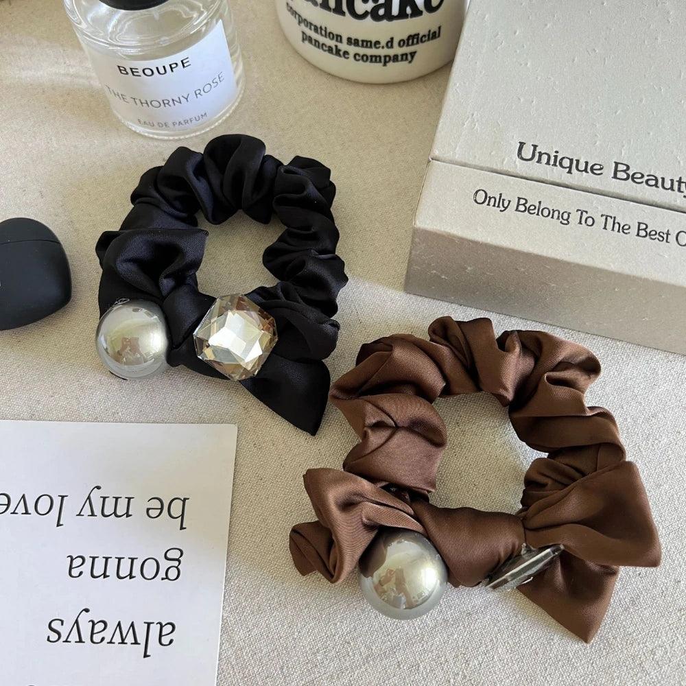 Close-up of black and brown satin scrunchies with metallic sphere and crystal embellishments