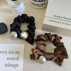 Close-up of black and brown satin scrunchies with metallic sphere and crystal embellishments
