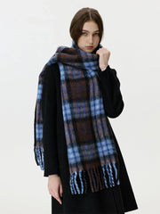 Close-up of a woman adjusting a blue and brown plaid scarf with fringe.