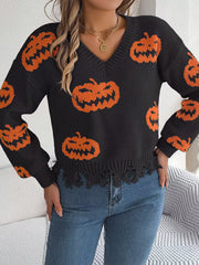Front view of a woman wearing a black long-sleeve v-neck cropped knit sweater with an all-over orange pumpkin print and a distressed hem, hands on hips.