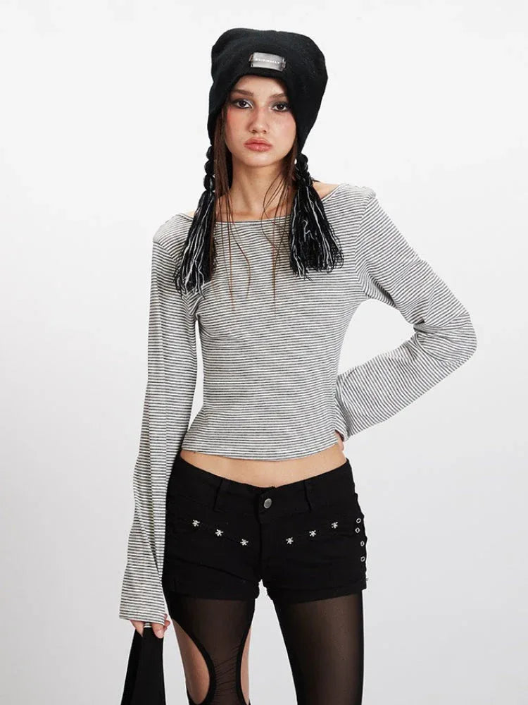 Front view of a model wearing a grey and white striped long-sleeved cropped top with flared sleeves, black shorts with cut-outs, black and grey striped thigh-high socks, and black sneakers. She is also wearing a black beanie.