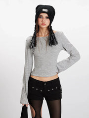 Front view of a model wearing a grey and white striped long-sleeved cropped top with flared sleeves, black shorts with cut-outs, black and grey striped thigh-high socks, and black sneakers. She is also wearing a black beanie.