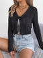 Woman wearing a black cropped knit cardigan with a tie front closure and denim shorts, seated on a couch.