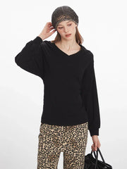 Close-up of a woman wearing a black V-neck long-sleeved top and leopard print wide-leg pants, with her hand touching her neck.