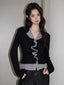 Woman wearing a black long-sleeved top with grey ruffled trim and dark wash wide-leg jeans.