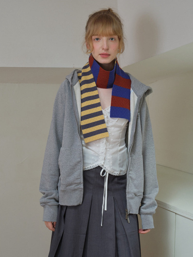 Model wearing a white lace camisole, grey zip-up hoodie, grey pleated skirt, and a striped scarf.