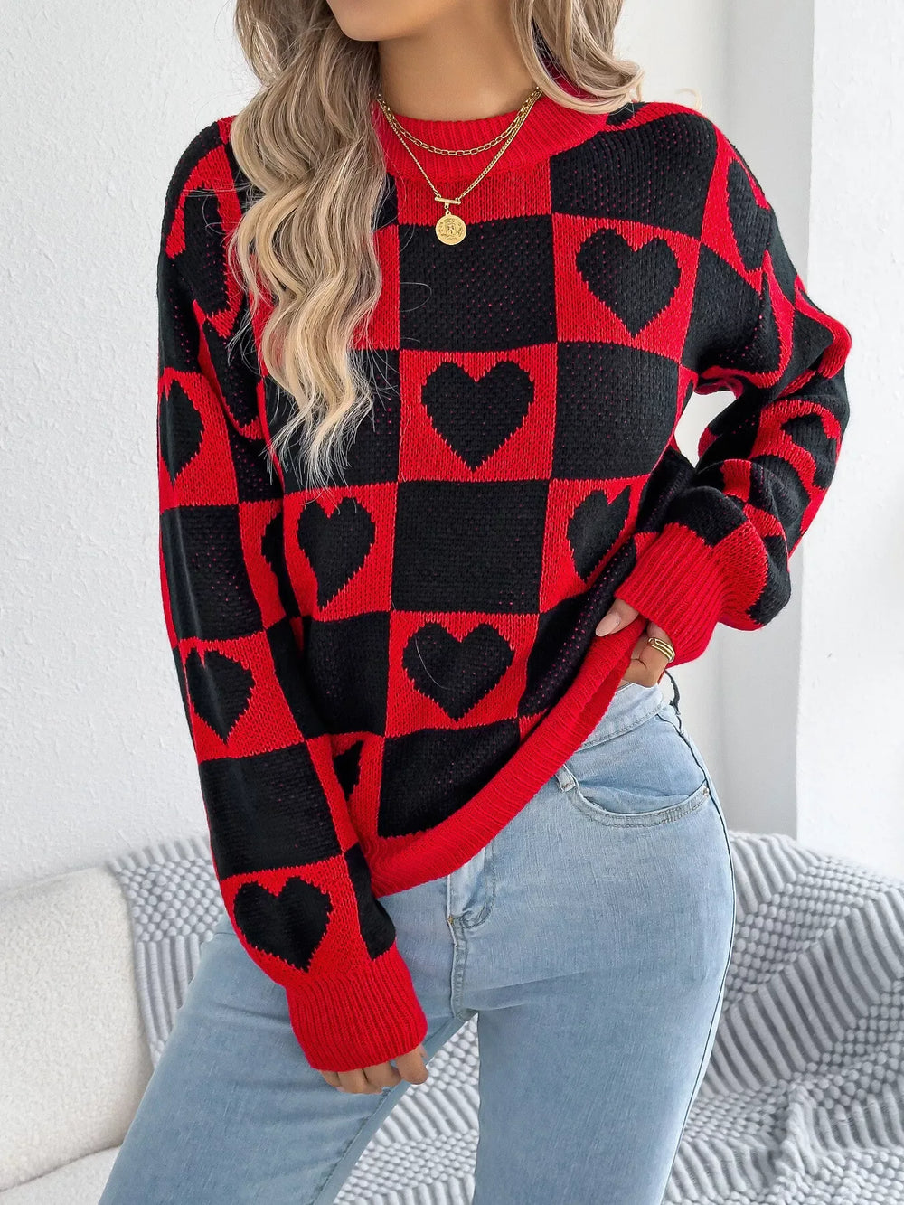 Close-up of a woman wearing a red and black checkerboard heart print knitted sweater with light blue jeans