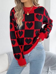 Close-up of a woman wearing a red and black checkerboard heart print knitted sweater with light blue jeans