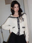 Woman wearing a white knit cardigan with black trim and a sailor collar, paired with a black skirt.