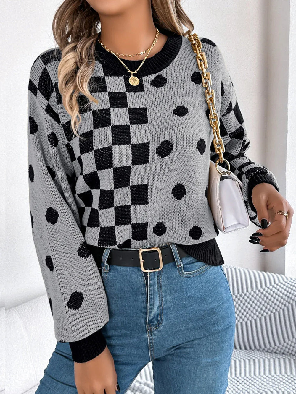 Woman holding a white handbag and wearing a gray and black checkerboard and polka dot knit sweater