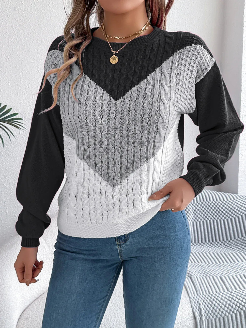Woman holding the hem of a black, grey, and white color block chevron cable knit sweater.
