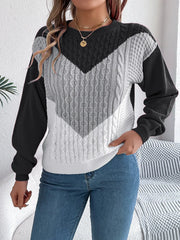 Woman holding the hem of a black, grey, and white color block chevron cable knit sweater.